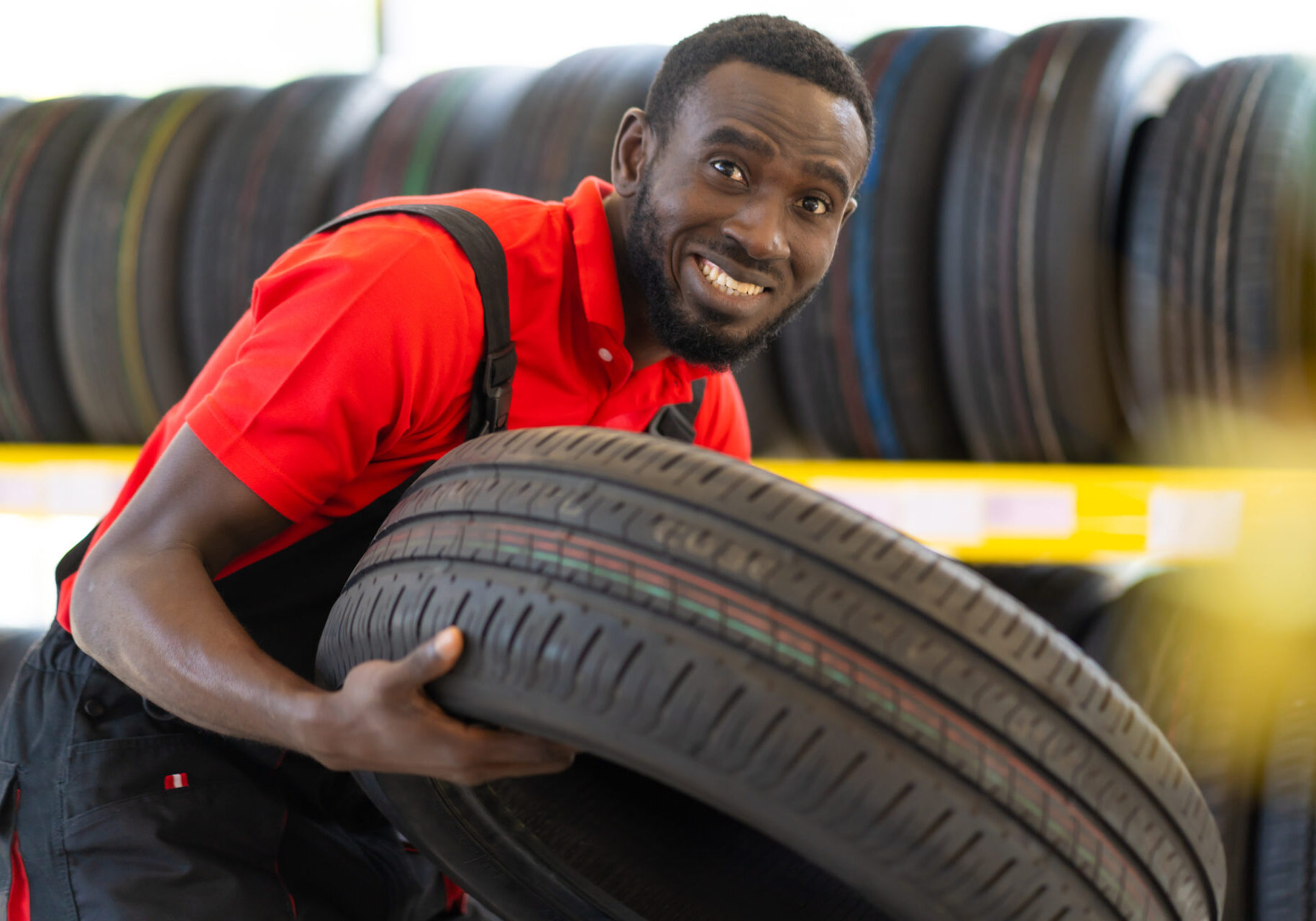 Black male Mechanic holding a tire and showing wheel tires at car repair service and auto store shop. Expertise mechanic working in automobile repair garage.